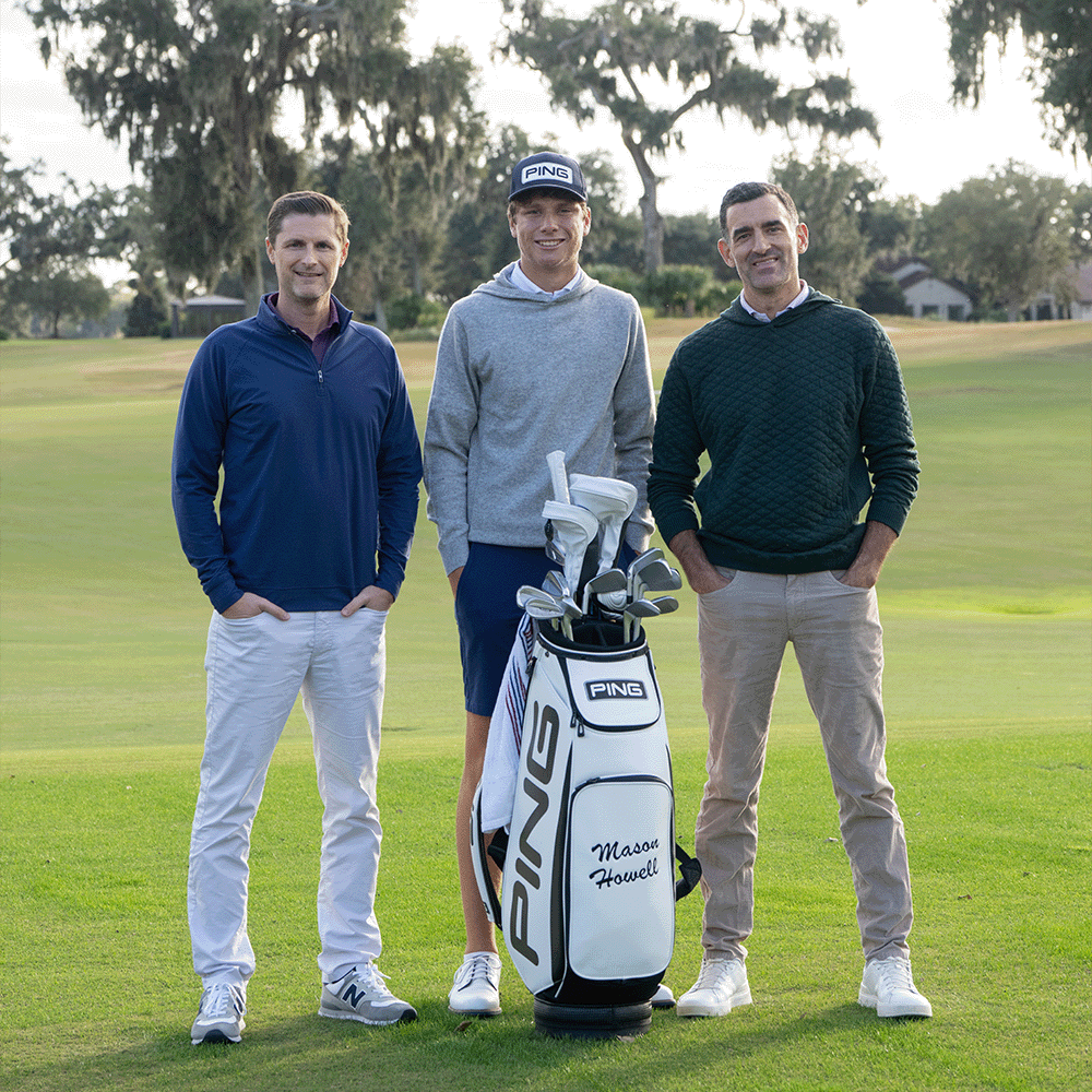 Three men standing on a fairway around a white PING bag marked "Mason Howell", wearing quarter-zips and sweaters.