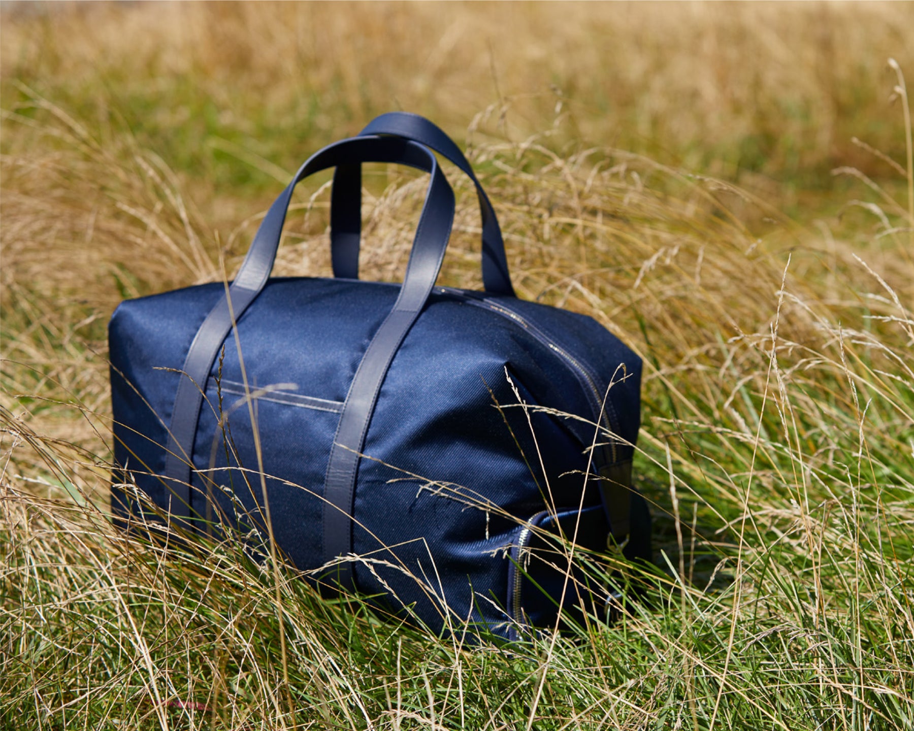 Navy bag from Holderness and Bourne atop an overgrown green field. 
