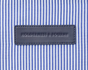 Close up of Holderness and Bourne logo on banker blue bag leather against striped fabric background.