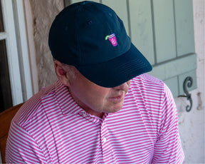 Man wearing navy performance golf hat with Holderness and Bourne logo and striped pink polo.