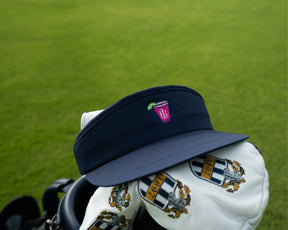 Holderness and Bourne navy visor golf with branded pink cocktail logo perched on top of golf clubs.
