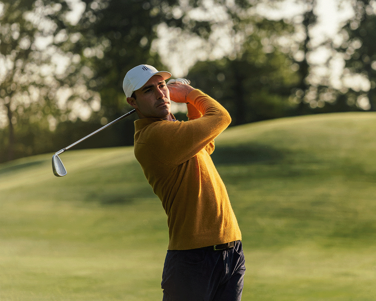 Man playing golf on a green course with trees in the background