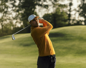 Man playing golf on a green course with trees in the background