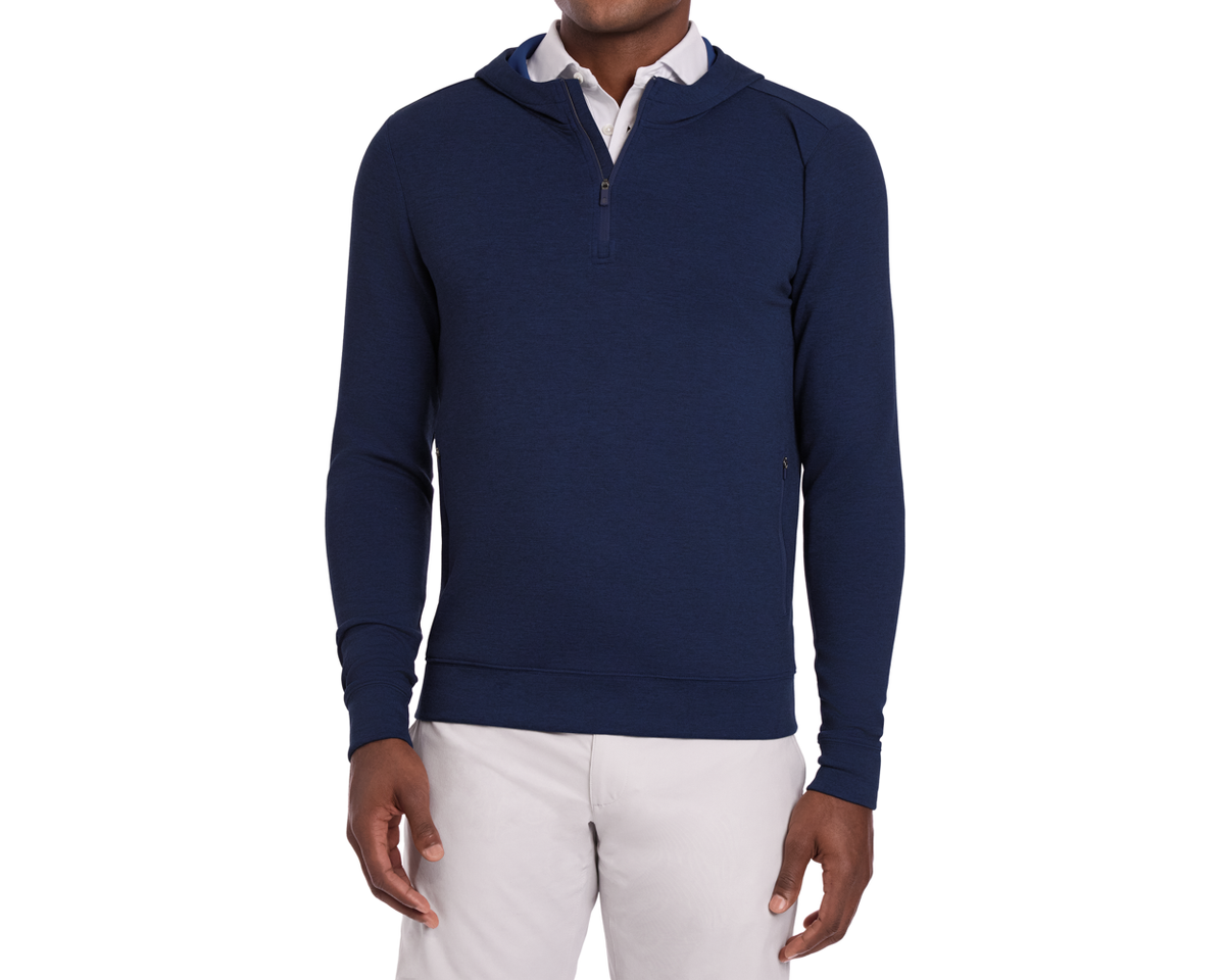 Man wearing The Tilley Quarter-Zip Hoodie: Heathered Navy, showcasing its sleek silhouette over a white collared shirt, paired with light trousers.