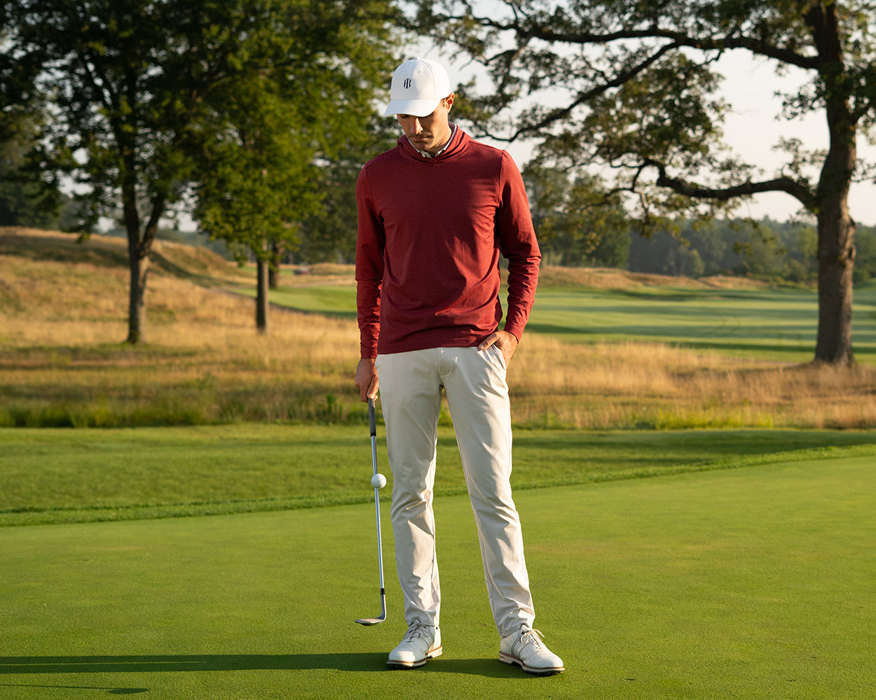 Man on a golf course wearing Holderness & Bourne Men’s Burgundy Hoodie preparing to putt with trees in the background