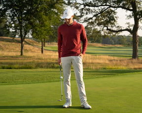 Man on a golf course wearing Holderness & Bourne Men’s Burgundy Hoodie preparing to putt with trees in the background