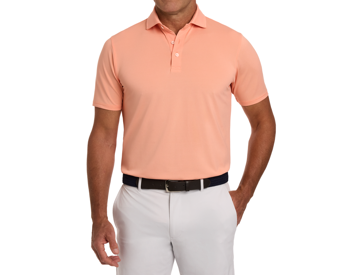 The Macdonald Shirt: Nectarine, worn by a male model, showcases a stylish pique design with a structured collar, tucked into light trousers with a dark belt.