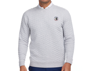 Man wearing 2026 U.S. Open Ward Sweater in heathered gray with diamond quilting, over white shirt, featuring U.S. Open patch; paired with navy trousers.