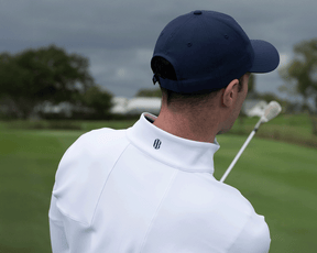 Man on golf course wearing 2026 U.S. Open Rodgers Pullover: White, holding golf club over shoulder, showcasing pullover's high collar and logo detail.