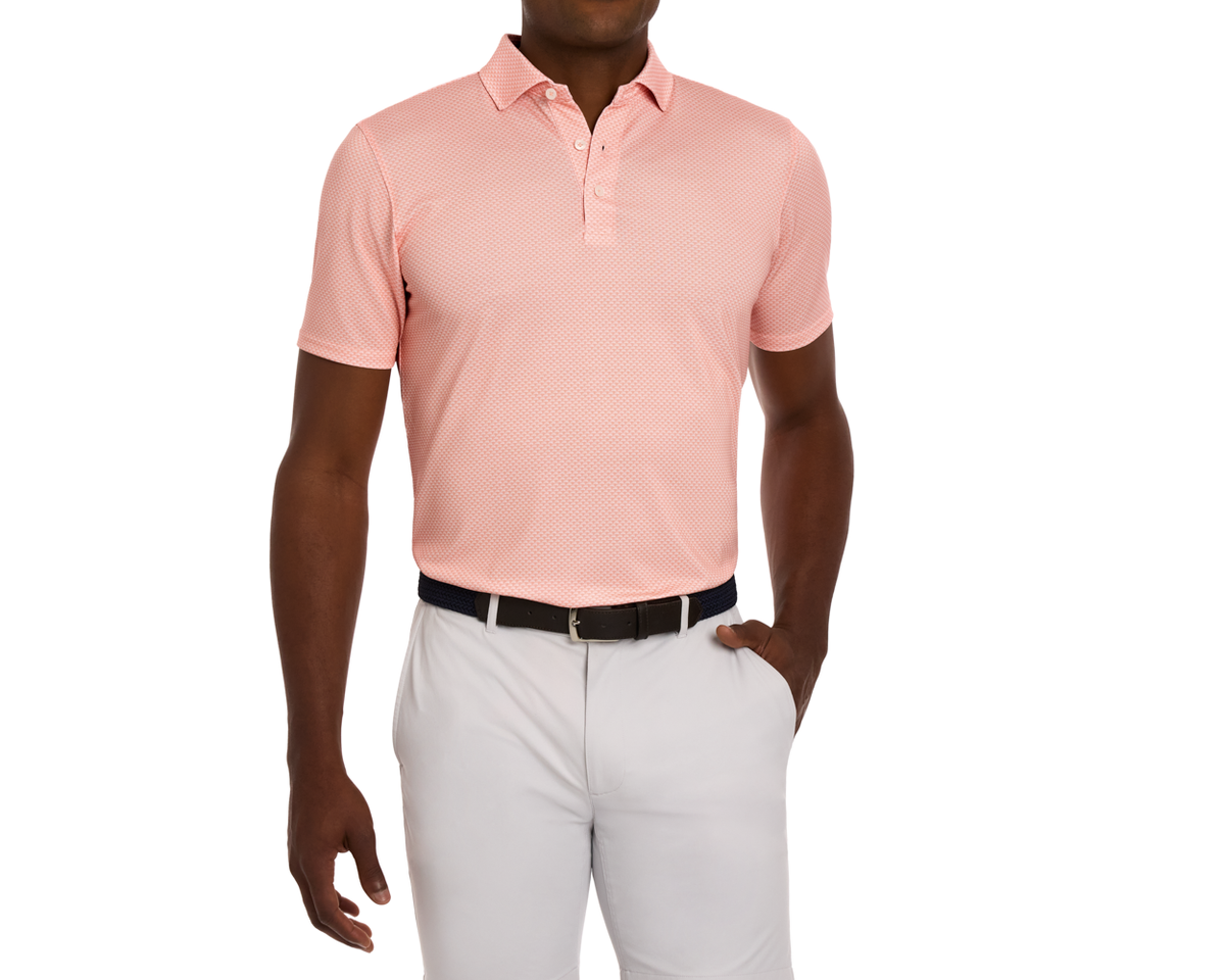 Male model wearing The Eaton Shirt: Nectarine, a short-sleeve polo with abstract wave pattern, tucked into gray trousers, accessorized with a black woven belt.
