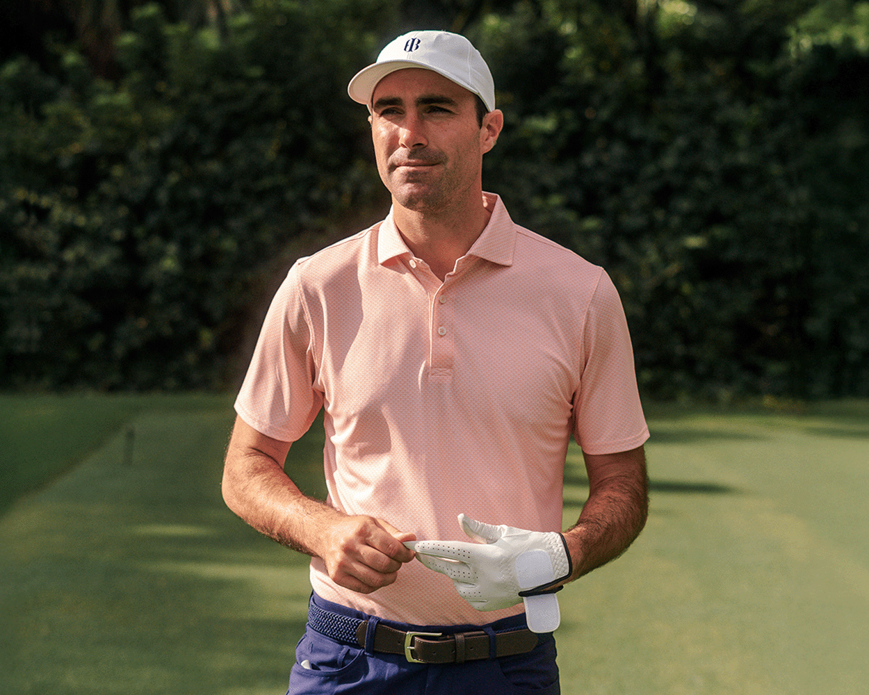 Man on golf course in The Eaton Shirt: Nectarine, adjusting glove. Features structured collar, abstract pattern, designed for comfort, moisture wicking, and sun protection.