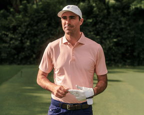 Man on golf course in The Eaton Shirt: Nectarine, adjusting glove. Features structured collar, abstract pattern, designed for comfort, moisture wicking, and sun protection.