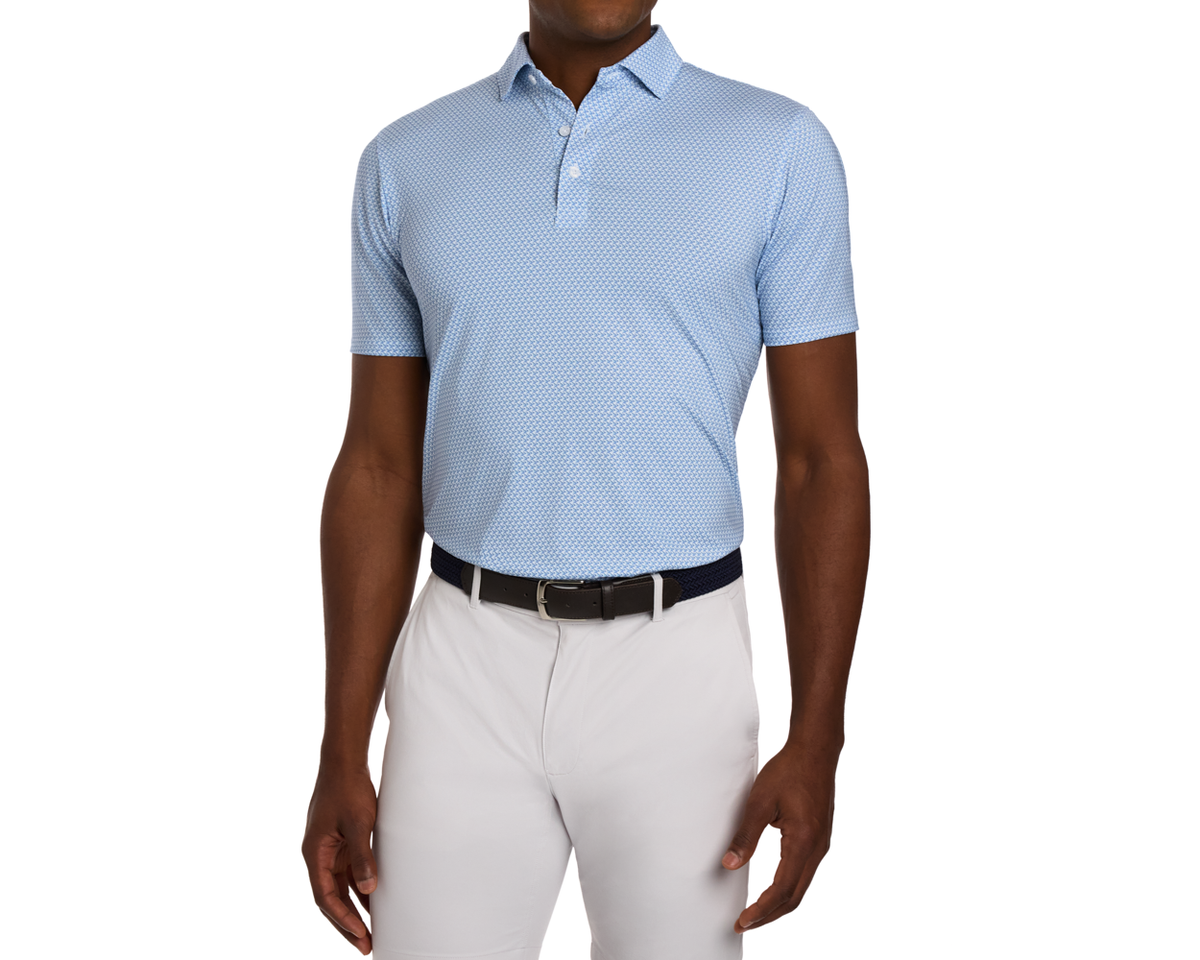 Male model wearing The Justice Shirt: Harbor & Maidstone Blue, a geometric print polo, tucked into light gray golf pants with a dark belt.
