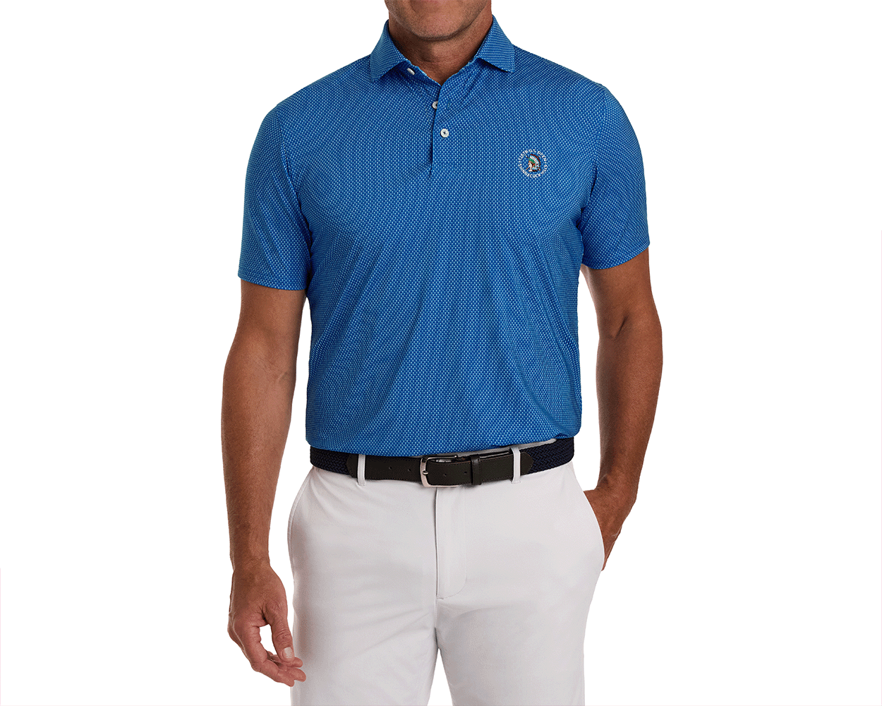 Man wearing the 2026 U.S. Open Hicks Shirt: Maidstone Blue, featuring a geometric dot print, embroidered logo, white trousers, and a dark woven belt.
