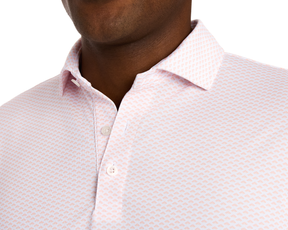 The Geiger Shirt: Nectarine features a light pink collared design with a small dot pattern, showcasing white buttons and breathable, moisture-wicking pique fabric.