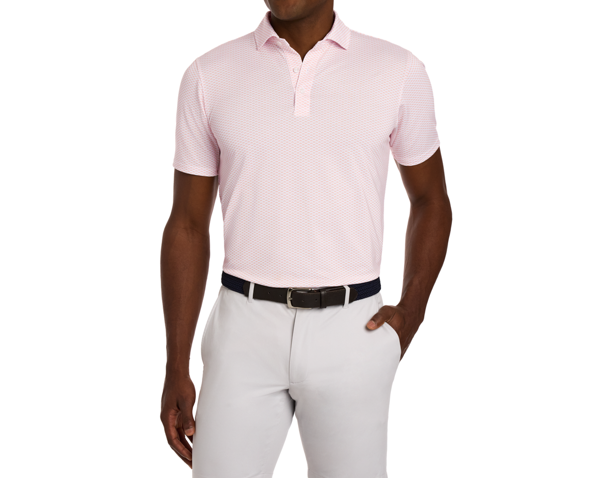 Man wearing The Geiger Shirt: Nectarine, a short-sleeve polo with abstract pattern, tucked into light trousers, featuring a woven belt.