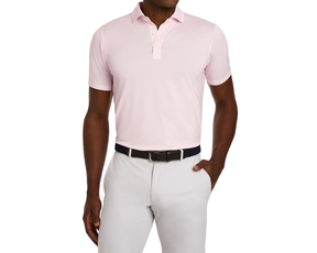 Man models The Geiger Shirt: Nectarine, a light-pink polo with abstract pattern, paired with light gray pants and dark woven belt, showcasing its breathable, moisture-wicking fabric.