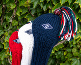 Red, white, and blue jan craig headcovers with embroidered Holderness and Bourne patch against green leafy background.