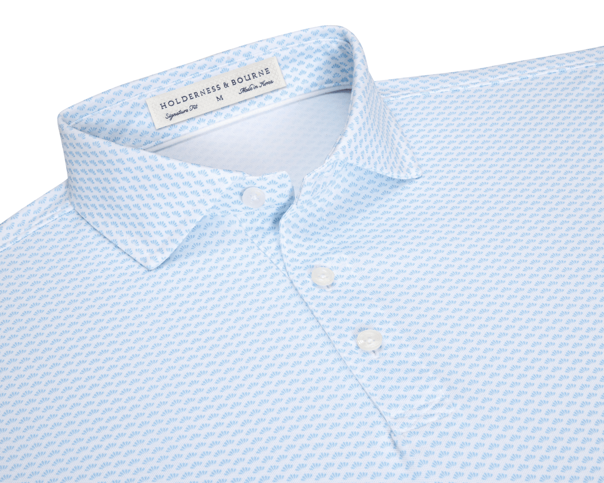 The Geiger Shirt: Vista Blue features a light-blue knit with a shell pattern, two-button placket, and spread collar, offering breathable, moisture-wicking performance.