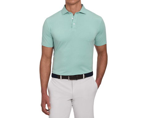 Model wearing The Holland Shirt: Heathered Cascade Green, featuring a heathered finish and short sleeves, paired with a woven belt and light gray pants.