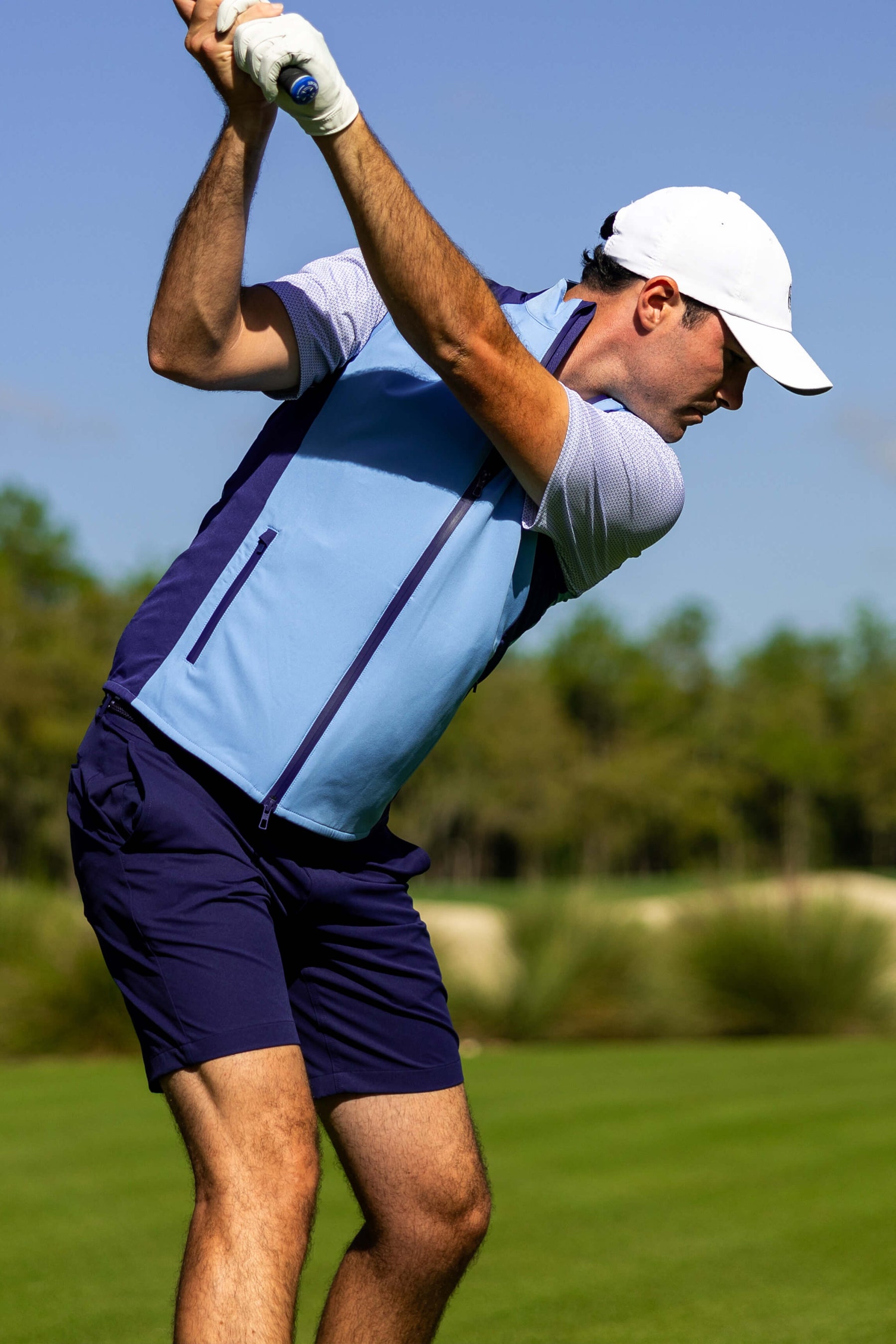 Golfer wearing Blue Vest and Shorts swinging a club