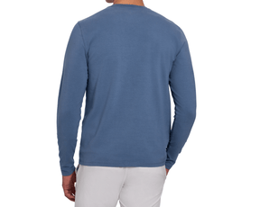 Back view of a male model wearing The Montague Long Sleeve T-Shirt: Pacific Blue, showing the plain back, long sleeves, and curved hem, with light gray pants.