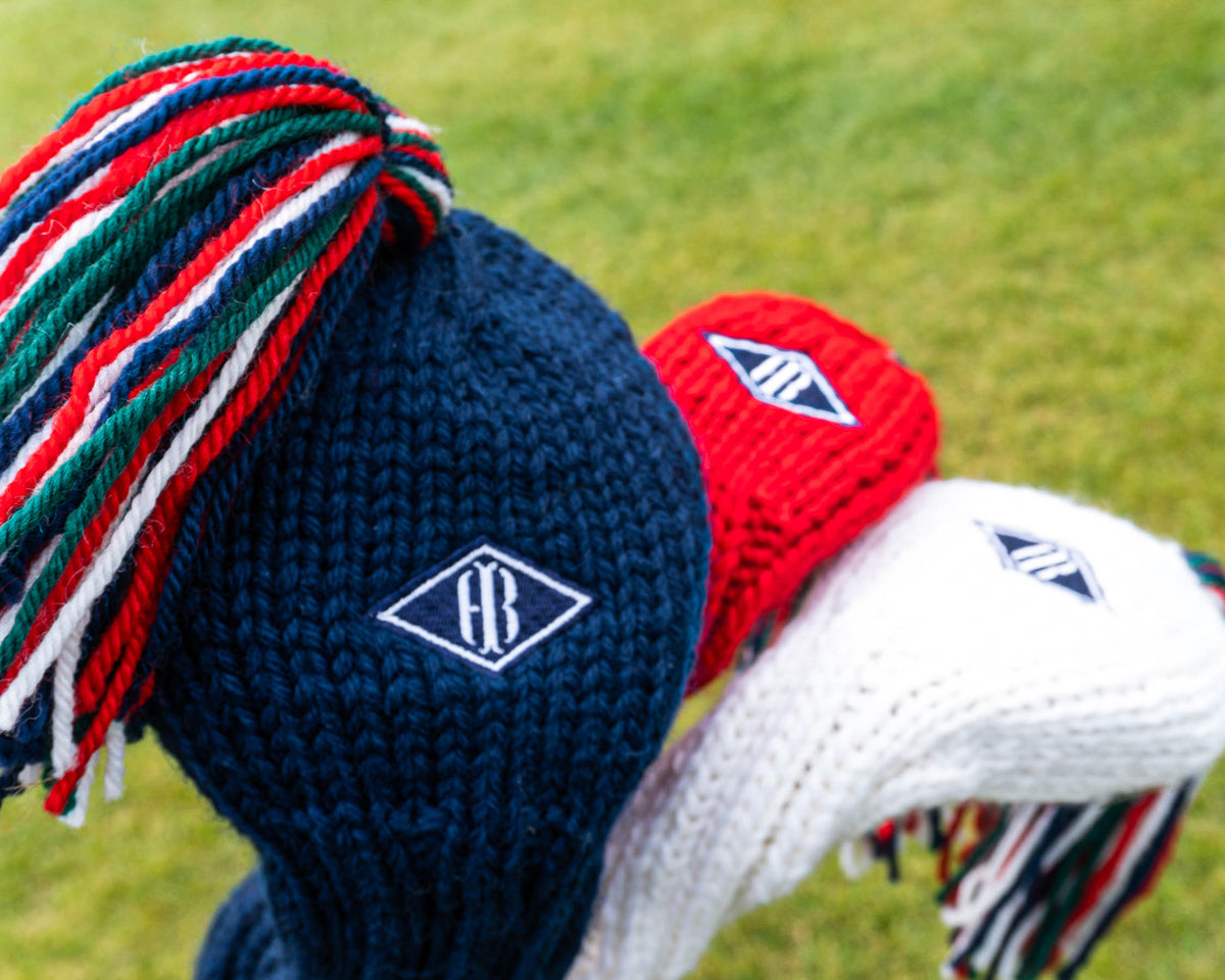 Red, white, and blue jan craig headcovers with embroidered Holderness and Bourne patch against grassy background.