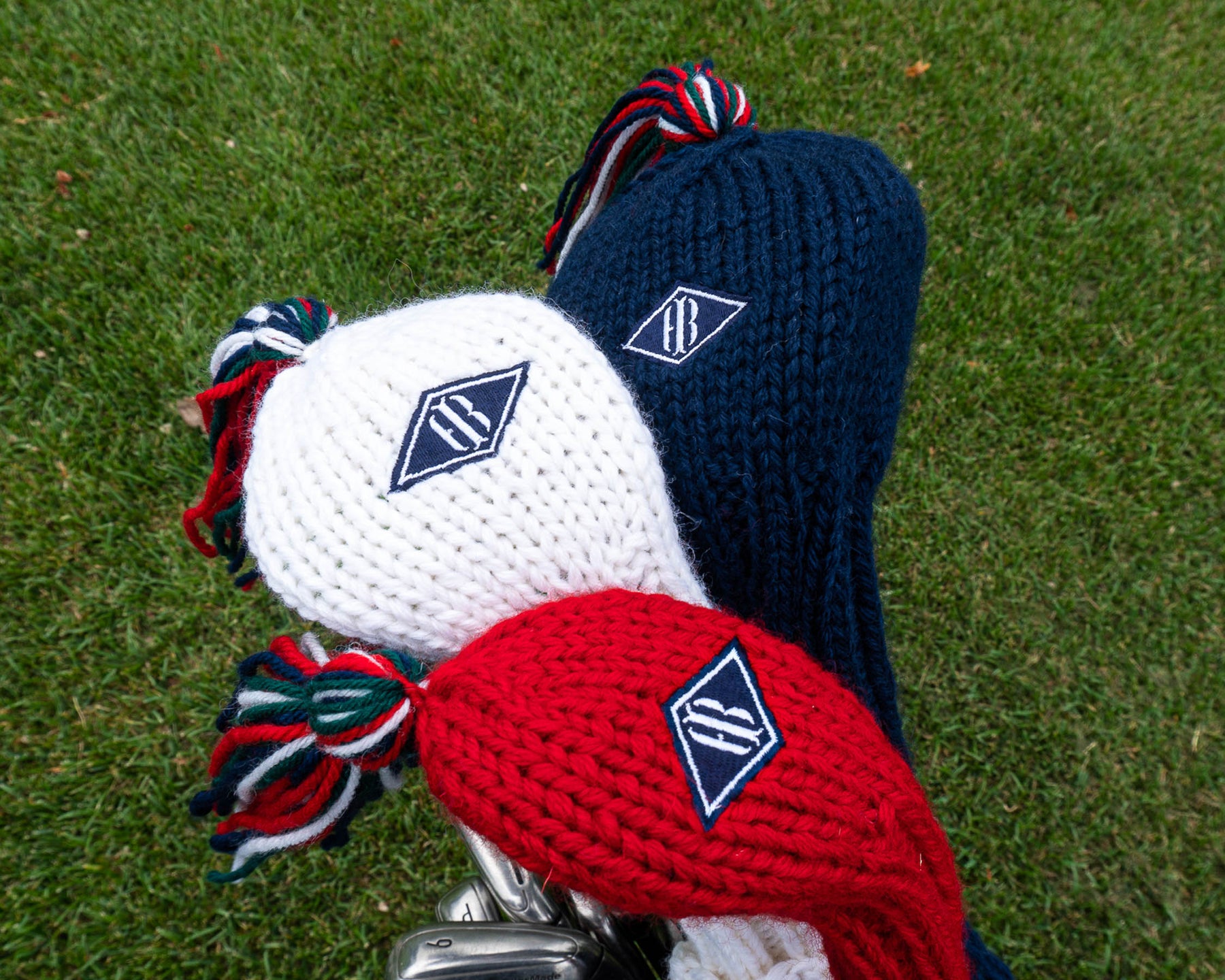 Red, white, and blue headcover set with embroidered Holderness and Bourne patch against grassy background.