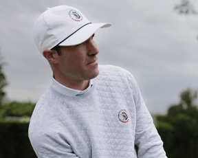 Man in 2026 U.S. Open Ward Sweater: Heathered Gray, featuring a quilt-textured pattern and logo, stands outdoors focused on his golf shot.