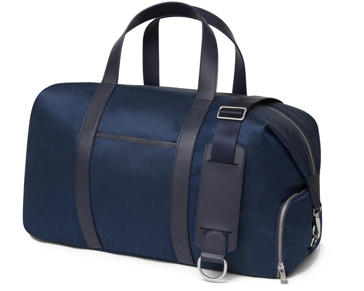 Navy duffle bag with dark leather straps and detailing from Holderness and Bourne angled to the left.