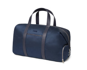 Navy embroidered sports bag with dark adjustable leather strap and embroidered lettering from Holderness and Bourne angled to the left.
