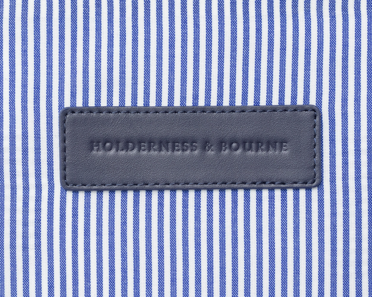Close up on Holderness and Bourne navy lettering against striped blue and white fabric background.