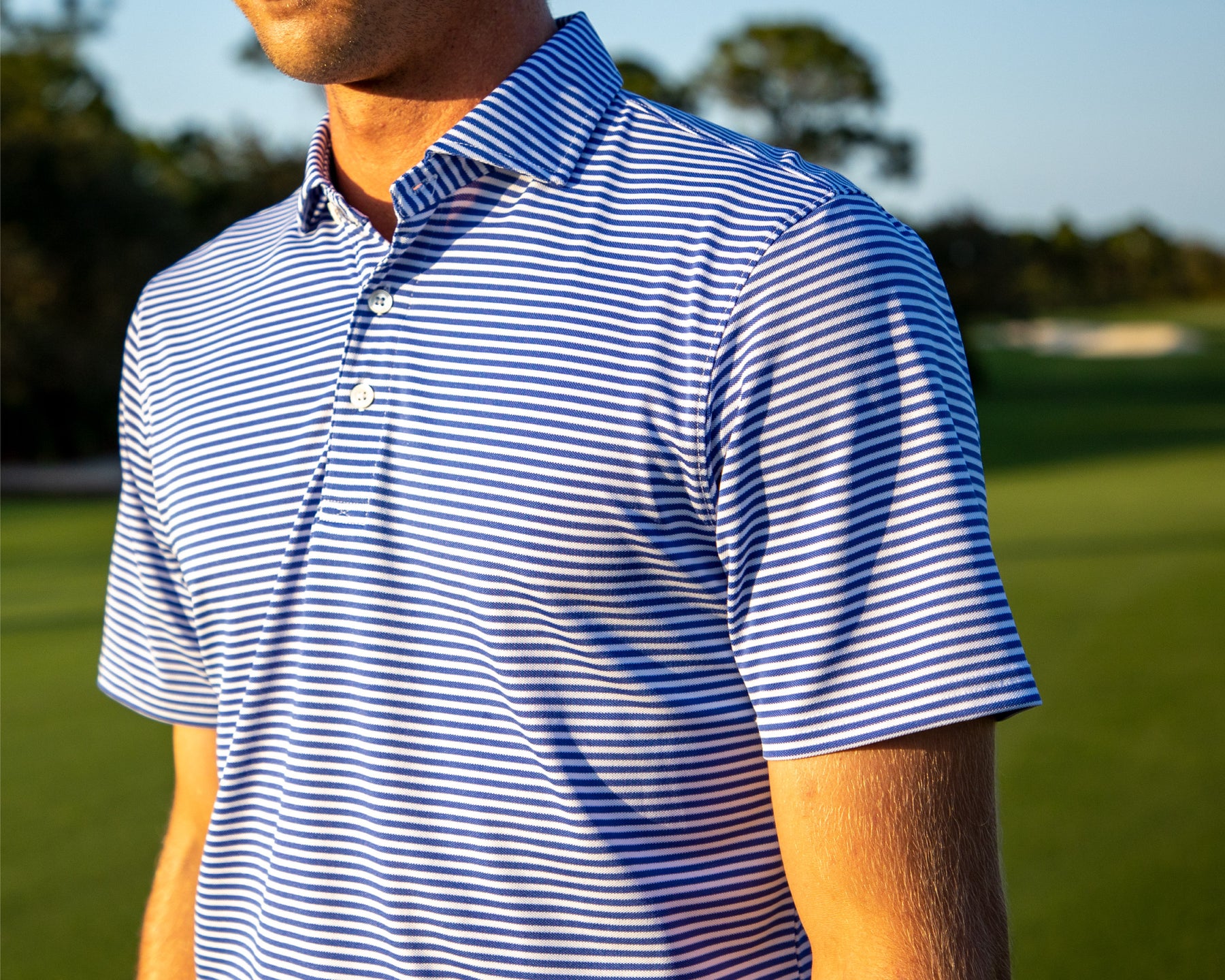 Man wearing Holderness and Bourne striped polo with golf course background.