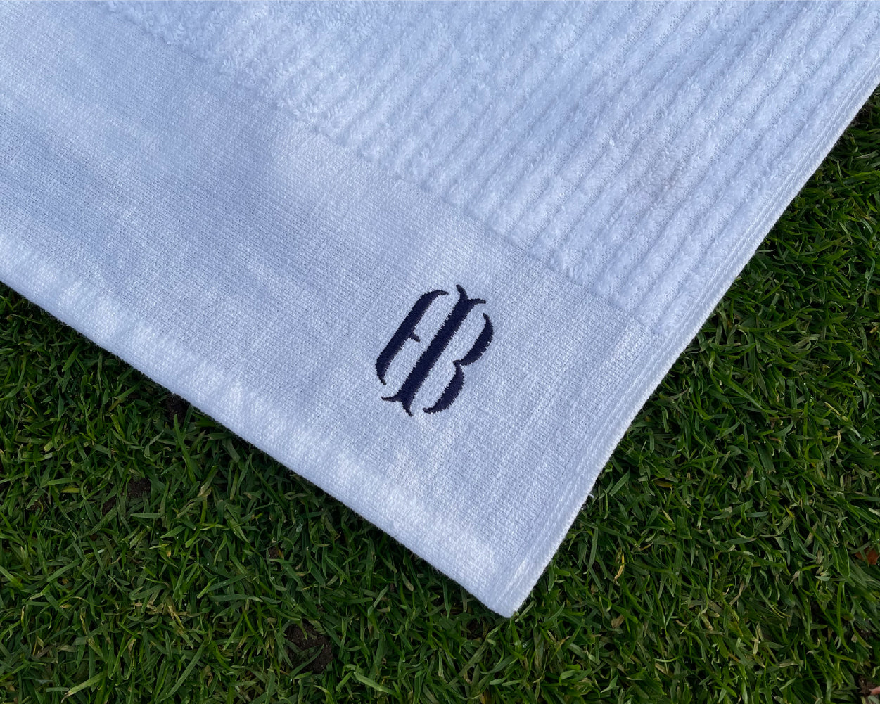 Close up on embroidered Holderness and Bourne logo on white and blue towel against grassy background