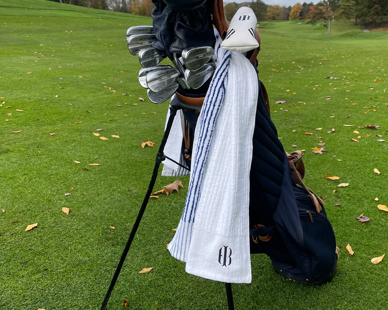 Holderness and Bourne blue and white towel drapes off of golf club bag on golf course.