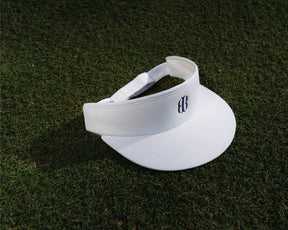 Blank white visor with navy Holderness and Bourne embroidered logo angled to the right on top of grass field.