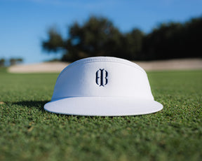 Blank white visor with navy Holderness and Bourne embroidered logo on top of grass field.
